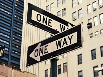 Two one way signs at a corner pointing in different directions